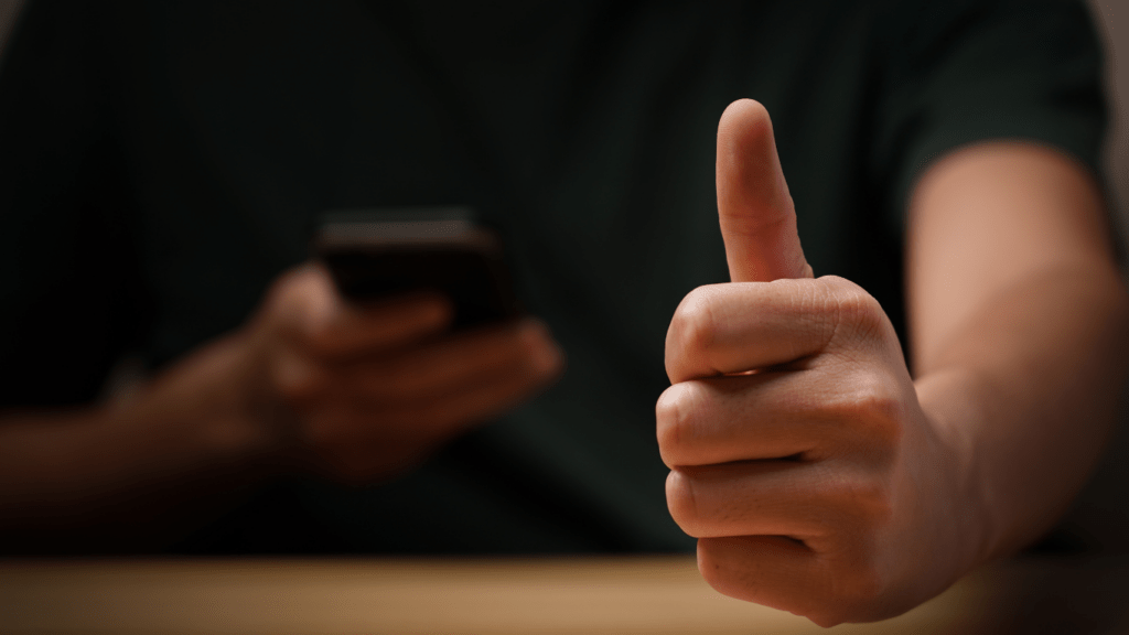 a person giving the thumbs up with a cell phone in front of them