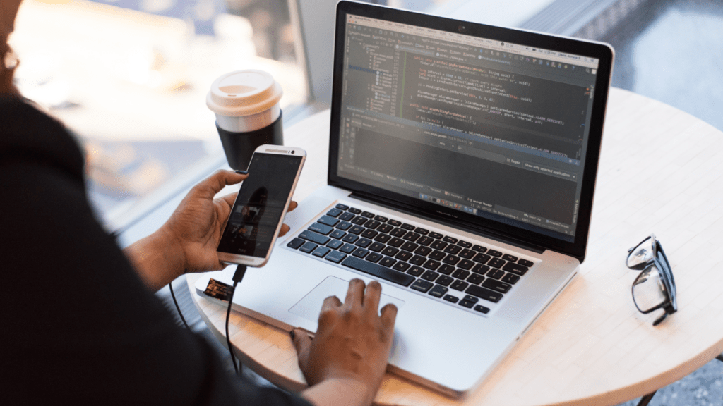 a person working on a laptop with a smartphone and a cup of coffee in front of it